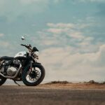 A Royal Enfield motorcycle parked on a scenic road with a clear blue sky backdrop.